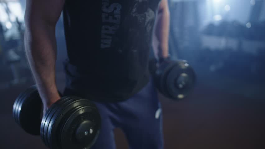 Caucasian man working out in the gym with dumbbells. An athlete pumps up his muscular arms while lifting a heavy weight. Workout and fitness is a healthy lifestyle.