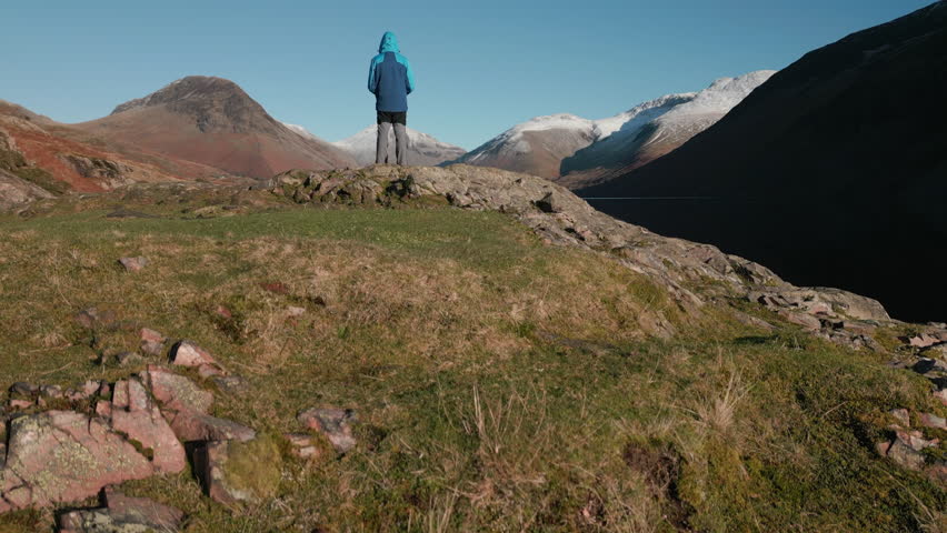 Mountain valley lake reveal surrounded by snow capped mountains with hiker at Wasdale Lake District UK