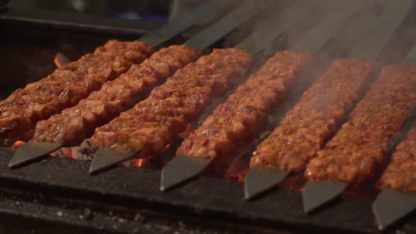 Various raw traditional Turkish skewers Adana Kebab made of meat lined up on charcoal on a skewer barbecue.
