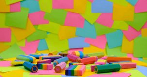 various shapes and colors of erasers arranged on a rotating table with multicolored paper sticky notes on background