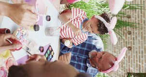 Vertical video of african american grandfather and grandson painting eggs for easter, slow motion. Easter, celebration, family, childhood and tradition concept.