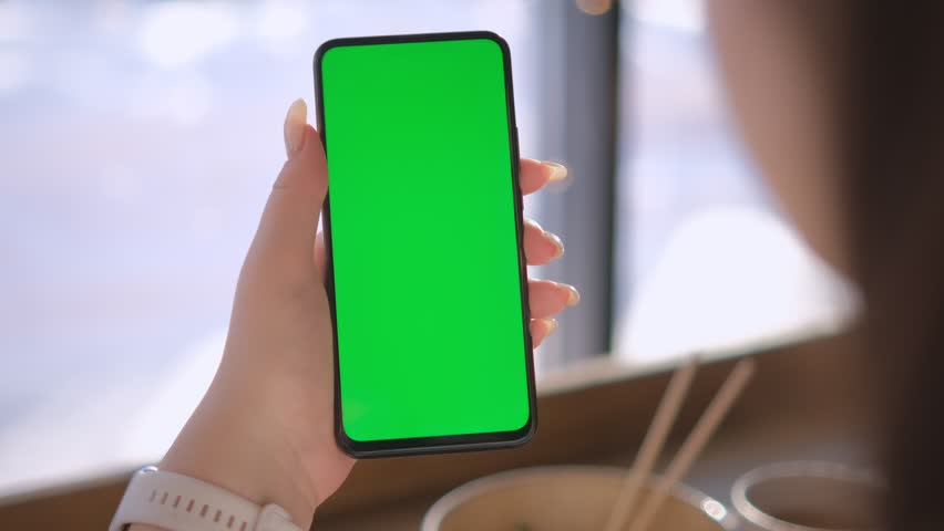 Young Woman in a chinese restaurant Sitting on a Couch with Green Screen Smartphone in Vertical Mode. Girl Using Smartphone, Browsing Internet, Watching Video Content, Blogs. POV. 4K | Shutterstock HD Video #1100503763