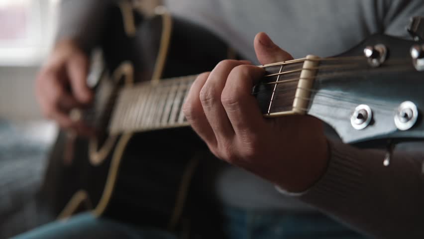 Playing the guitar. Strumming black acoustic guitar. Musician plays music. Man fingers holding mediator. Male hand playing guitar neck in dark room. Unrecognizable person rehearsing, fretboard closeup Royalty-Free Stock Footage #1100503823
