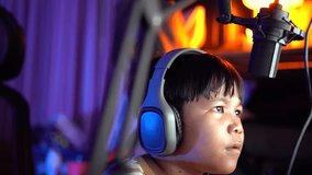 Close up of Boy talks looking to computer monitor screen. Kid wearing headphones using microphone. Online learning, remote education, gaming, podcast. 