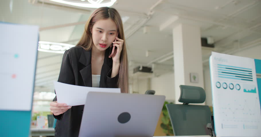 Young busy asian business woman working on project paperwork talking phone, using laptop remotely work in modern office. Female freelancer entrepreneur making distance job telesale call with customer. | Shutterstock HD Video #1100507441