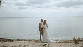 Beautiful newlywed couple posing to camera, the sea is in the background, slow motion. Video portrait of bride and groom in love.