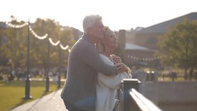Middle aged tourist couple exploring city. Senior man and woman hug on city bridge. Happy mature couple embrace standing on bridge in park. Aged husband and wife outdoors. Realtime - Powered by Shutterstock - Get 15% off with code: PIKWIZARD15