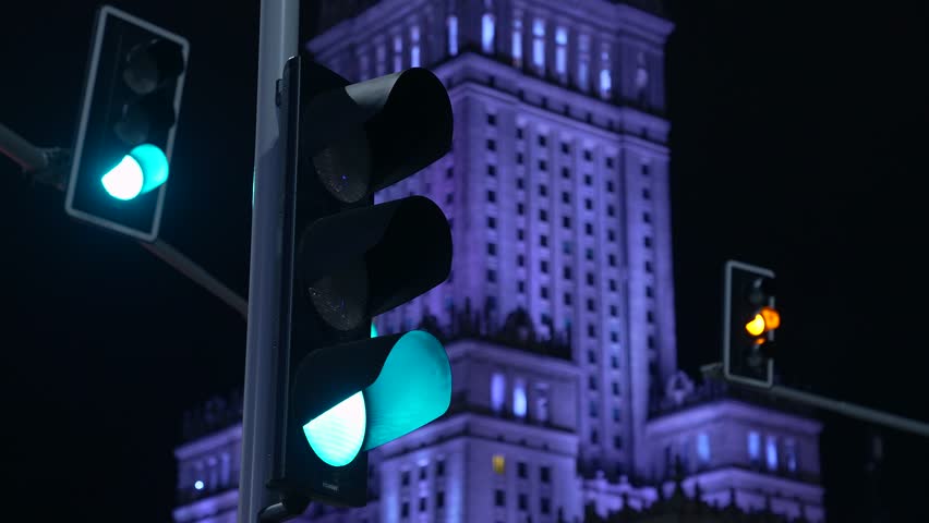 Night view of traffic light and Palace of Culture and Science. The traffic light switches from green to red. In the backlight highlighted purple color Palace of Culture and Science. Warsaw, Poland.