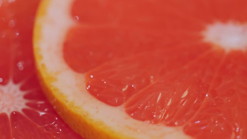Selective focus: colorful fresh red raw citrus fruit slices of grapefruit on rotating surface - close up view, macro. Summer, tropical, natural, exotic and healthy food concept