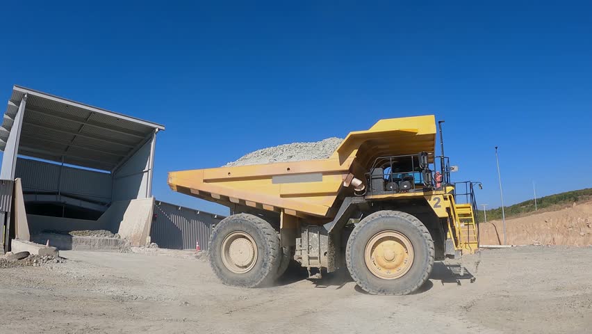 Big yellow mining truck at work site unloading ore in production facility, slow motion