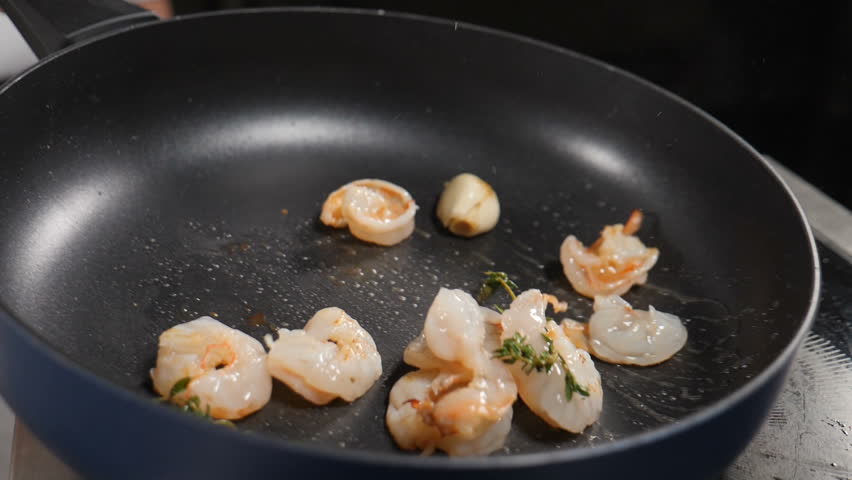 Restaurant kitchen. Chef tosses deep-fried shrimps in frying pan on black background. Chef tossings, mixing and throwing on pan prawns, close-up slow motion. Full hd | Shutterstock HD Video #1100514053