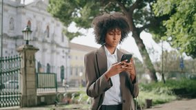Focused woman surfing internet on smartphone standing alone at city park closeup. Attractive serious african american business lady typing phone message outdoor. Pretty girl using mobile on work break - Powered by Shutterstock - Get 15% off with code: PIKWIZARD15