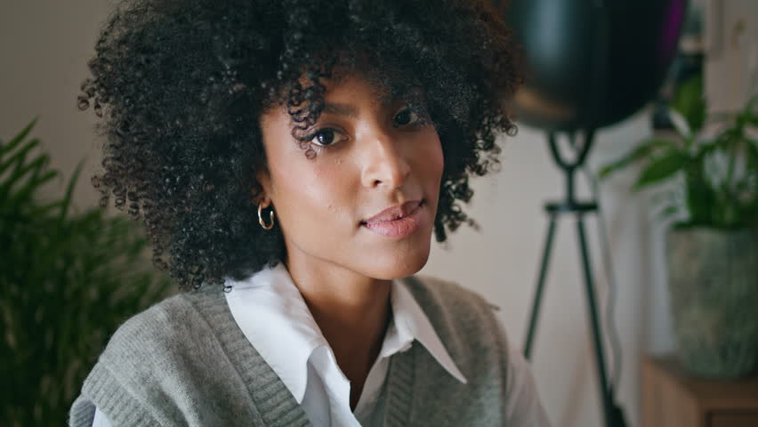Portrait of beautiful relaxed african american brunette sitting at cozy interior. Pensive attractive woman looking camera with calm smile close up. Curly gorgeous girl posing relaxing in modern cafe. | Shutterstock HD Video #1100516287