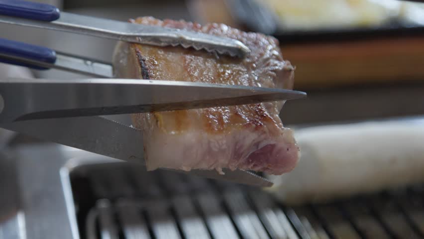 Cut well-cooked Korean pork belly with scissors. Cut pork belly is piled up on the grill. Royalty-Free Stock Footage #1100522853