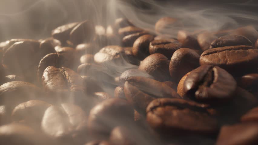 Process of roasting coffee beans. Smoke comes from fresh coffee seeds.Sliding shot of roast coffee beans with smoke on dark background Royalty-Free Stock Footage #1100527639