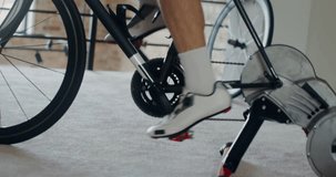 A man in sportswear and shoes for a bicycle trains on a bicycle simulator, practicing standing up riding. Close-up of male legs, dynamic video
