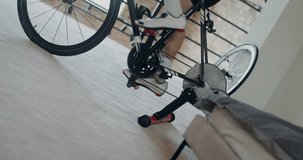 A young athletic man trains on a bike simulator, practicing standing up riding. Indoor cycling in a modern home interior. Dynamic video from the side