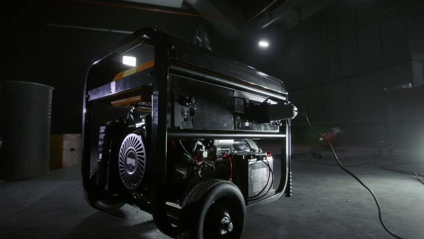 Black mobile gasoline power generator in a dark workshop. Gasoline powered generator that produces light. Battery equipment connected by wires. Dark empty room with light. Royalty-Free Stock Footage #1100532709