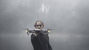 Caucasian man flies a drone in front of a lake in a cloudy forest