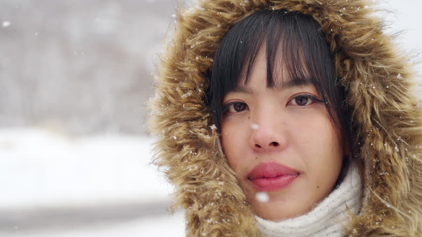 4K Close up of Young Asian woman face in winter coat walking down small town street in snow day. Attractive girl tourist solo travel local village covered in snow in Japan on winter holiday vacation.