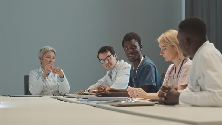 Waist up shot of diverse medical team having meeting with mid adult Asian female chief doctor sitting at head of table in modern conference room - Powered by Shutterstock - Get 15% off with code: PIKWIZARD15