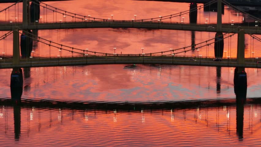 Roberto Clemente, Andy Warhol, and Rachel Carson bridges during orange sunset reflection on Allegheny river. Long aerial zoom and tilt up. Pittsburgh yellow bridges establishing shot.
