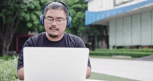 Asian freelance working in headphones and working on laptop in the outdoors with high speed internet. Online meeting via video call and presentation work