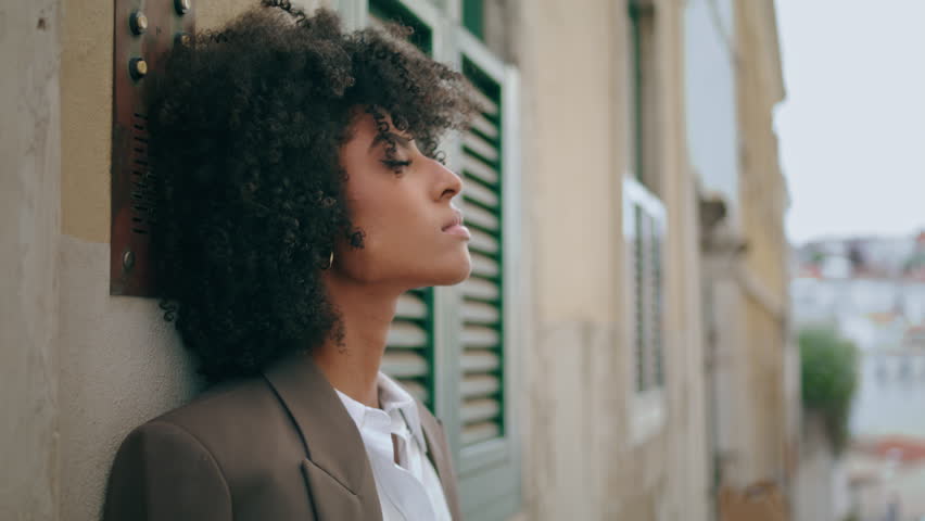 Relaxed african american lady standing city street leaning on wall close up. Portrait of attractive calm woman looking camera tired after long walk. Stylish pretty model posing outdoors. Town leisure. | Shutterstock HD Video #1100539043