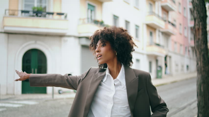 Stylish attractive business woman catching taxi standing city street close up. Confident curly african american girl waving hand to take car. Beautiful young lady wearing elegant jacket posing in town Royalty-Free Stock Footage #1100539065