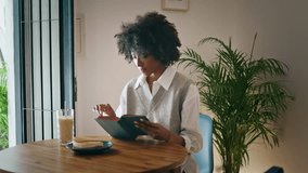 Curly young girl turning book page sitting at wooden table cozy cafe alone. Attractive african american woman reading interesting literature at breakfast in cafeteria. Relaxed brunette enjoying novel. - Powered by Shutterstock - Get 15% off with code: PIKWIZARD15