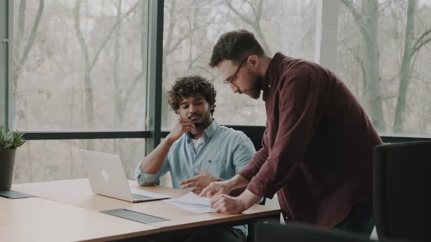 Two diverse businessmen planning working talking together at contemporary office using laptop. Multiethnic executive team discussing financial report sitting at table. | Shutterstock HD Video #1100540225