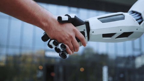 Robot and man shaking hands on sunny day outdoors. Future technology. Modern building on background. Agreement concept. Handshake of artificial intelligence and unrecognizable man. Robot arm วิดีโอสต็อก
