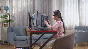 Asian Teen Girl Programmer Looking At Database On Tablet While Creating Software Engineer Developing App, Program, Video Game On Desktop Computer At Home
