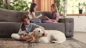 Little girls, children playing on sofa, hugging cute dog od golden retriever in the living room on daytime. Relaxation. Concept of family, childhood, pets, care, friendship, emotions. leisure