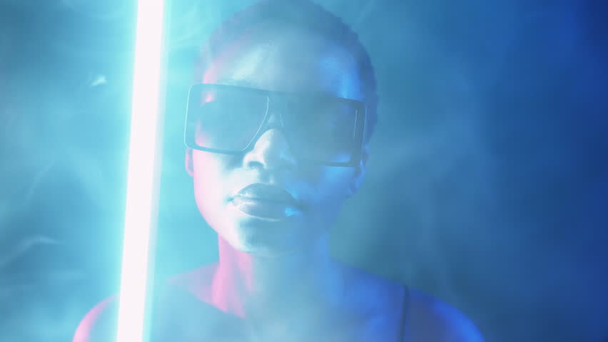 Eyewear fashion. Neon light face. Cyberpunk beauty. Blue red color mysterious girl posing in stylish sunglasses in smoke cloud at dark night with white LED lamp illumination.
