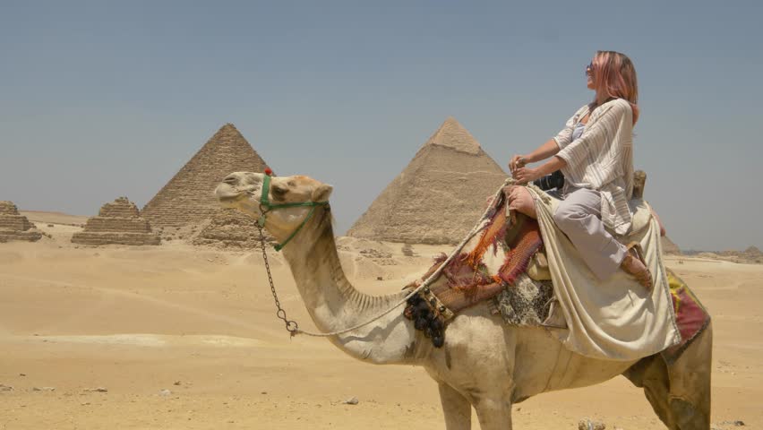 Egypt - circa 2022 - a woman rides a camel by the pyramids of giza.