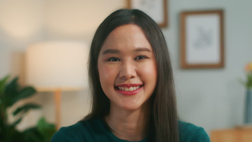 Portrait of beautiful asian woman charmingly smile looking at camera. Happy freelancer student sit on desk in living room at home office in casual outfits. Young adult female posing. close up face. | Shutterstock HD Video #1100553447