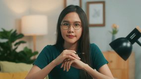 Confident Young Asian businesswoman looking at camera working and making meeting online video conference call focused on discussing with colleague presenting project holding pen pensile in living room