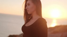 beautiful girl at dawn by the sea and rocks.portrait video of a girl at sunset
