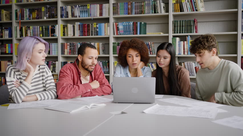 Team of students have fun together while doing homework in the library campus. They're sitting at desk with laptop, making researches on internet, browsing websites, preparing school project together Royalty-Free Stock Footage #1100568107