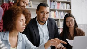 Close-up of an African American man, successful confident young professor and diverse teenage high school students working on laptop in the library campus. - Powered by Shutterstock - Get 15% off with code: PIKWIZARD15