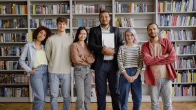 Full-length portrait of happy university graduate diverse students standing near professor and smiling looking at camera, posing against the background of bookshelves in library campus after lecture - Powered by Shutterstock - Get 15% off with code: PIKWIZARD15