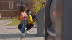 Father and little daughter throw empty bottle into recycling bin. African-American dad and child throw waste in city container. Family throwing waste in bin. Environment, ecology concept. Realtime - Powered by Shutterstock - Get 15% off with code: PIKWIZARD15