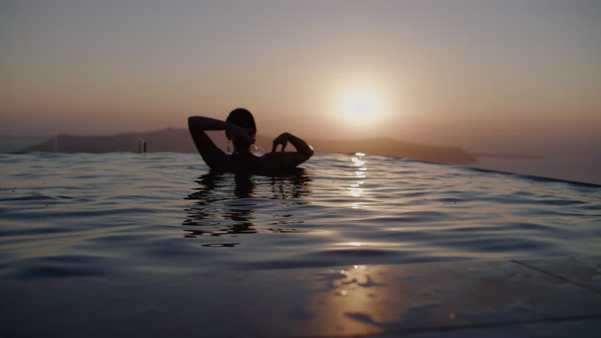 A woman dancing in infinity pool watching sunset over sea - Slow motion, Santorini, Greece Royalty-Free Stock Footage #1100570487