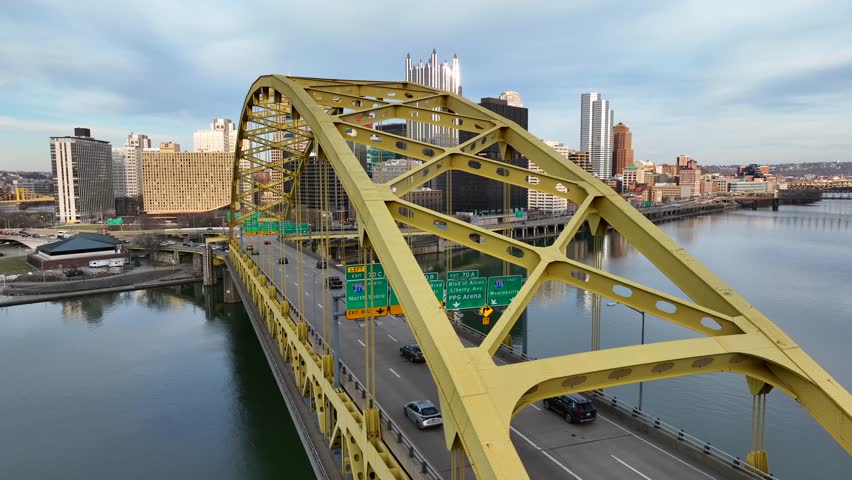 Fort Pitt Bridge in Pittsburgh Pennsylvania spans over Monongahela River. Sun shines on PPG glass castle skyscraper on skyline. Aerial establishing shot.