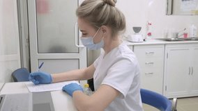 Young nurse wearing medical gloves and mask writes down information about the patient according to the doctor in hospital. Dentist assistant in white uniform sit at desk in dental clinic - Powered by Shutterstock - Get 15% off with code: PIKWIZARD15