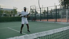 Athletic young black man in sports clothing hitting ball with tennis racquet while playing at sports court