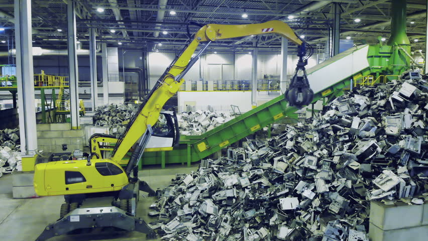 Trash, e-waste, electronic garbage recycling factory. Excavator grabs garbage and puts it onto factory conveyor. Royalty-Free Stock Footage #1100576337