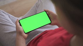 Point of View of Child at Living Room Using Phone With Green Mock-up. Phone With Green Mock-up Screen Chroma Key Surfing Internet Watching Content Videos Blogs Learning. Girl Playing Video Games.
