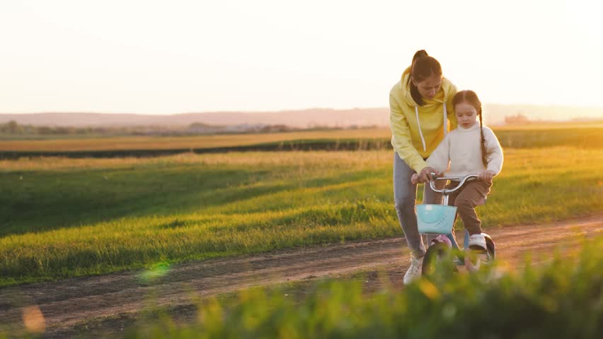mother teaches child ride two-wheeled bicycle sunset. fun weekend by bike. child's dream kid. child drive bicycle. mom rides girl child daughter bikerays sunset. happy family concept. teamwork. Royalty-Free Stock Footage #1100577097
